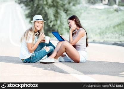 Happy young women with vintage music headphones and a takeaway coffee cup, surfing internet on tablet pc together and having fun against urban city background.