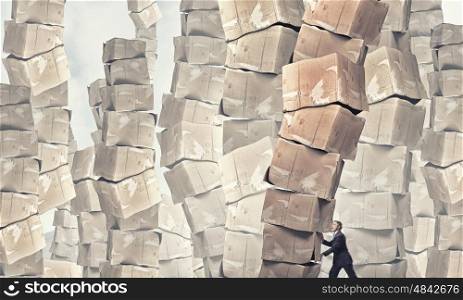 Hard career in business. Young businessman making effort to move stack of carton boxes