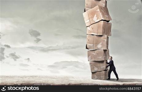 Hard career in business. Young businessman making effort to move stack of carton boxes