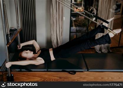 Hard workout in fitness studio. Motivated young fit woman pilates instructor doing strength exercise on cadillac reformer, showing power in every muscle movement. Active and healthy lifestyle. Young woman working hard on pilates reformer