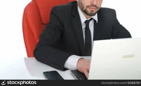 Hardworking businessman sitting at his desk working on his laptop computer frowning as he types information on the keyboard