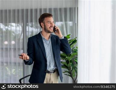 Hardworking businessman stand confidently in modern office making persuasive sales call to client. Office worker talking on the phone coordinate and manage business work with colleagues. Entity. Hardworking businessman stand in modern office talking on phone. Entity
