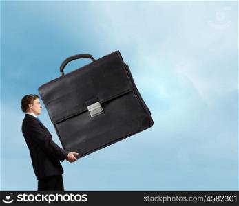 Hardworking businessman. Young determined businessman carrying big heavy suitcase