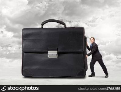 Hardworking businessman. Young determined businessman pushing big heavy suitcase