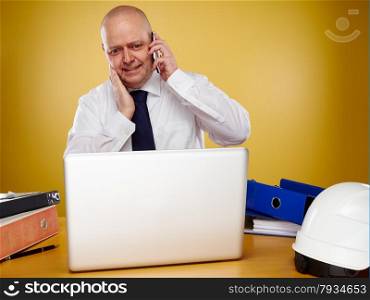 Hardworking male engineer in office, he wearing a white shirt and tie, the laptop, binders and white hard hat is on the table