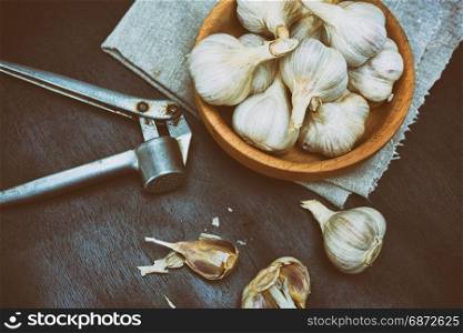 Harvest garlic in husk in a wooden bowl on a black background and iron press