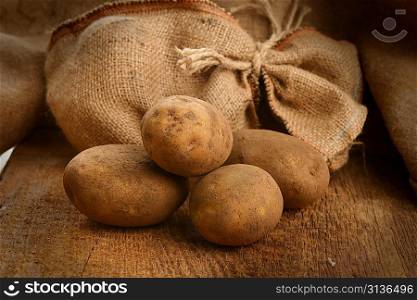 Harvest potatoes in burlap sack on wooden background