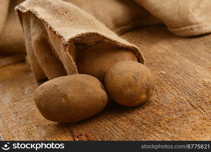 Harvest potatoes in burlap sack on wooden background