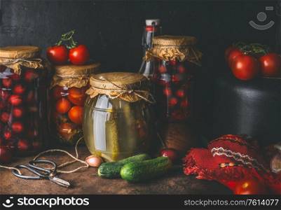 Harvest preserve concept. Glass jar with fermented pickled vegetables and fruits on dark rustic kitchen table with canned food for winter season. Canning and conservation of harvest.