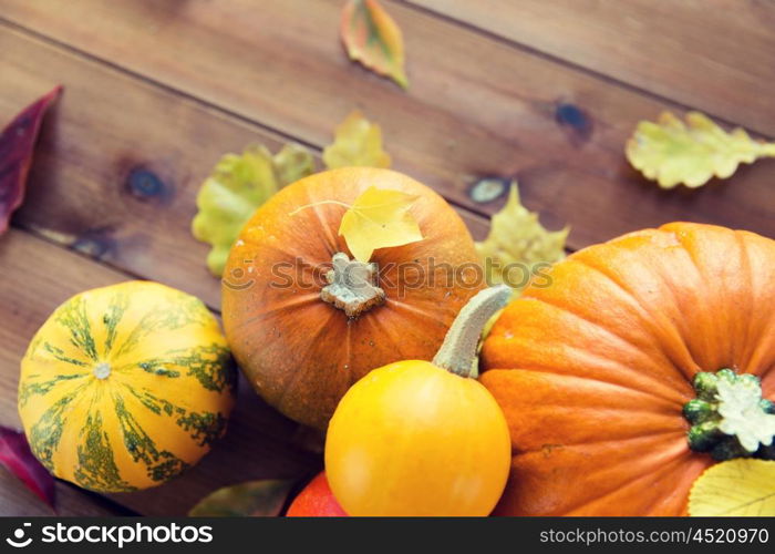 harvest, season, advertisement and autumn concept - close up of pumpkins and leaves on wooden table at home