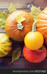 harvest, season, advertisement and autumn concept - close up of pumpkins and leaves on wooden table at home