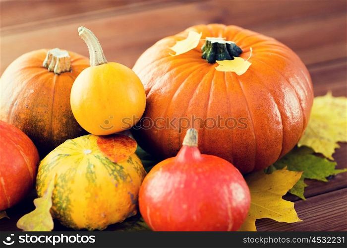 harvest, season, advertisement and autumn concept - close up of pumpkins and leaves on wooden table at home