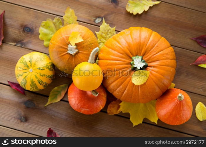 harvest, season, advertisement and autumn concept - close up of pumpkins and leaves on wooden table at home