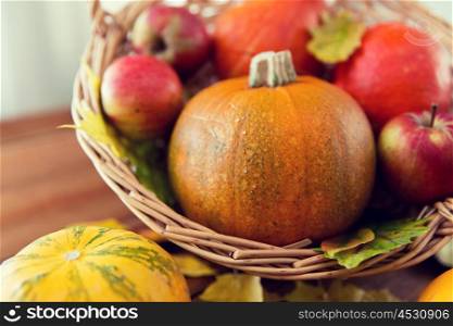 harvest, season, advertisement and autumn concept - close up of pumpkins in wicker basket with leaves on wooden table at home