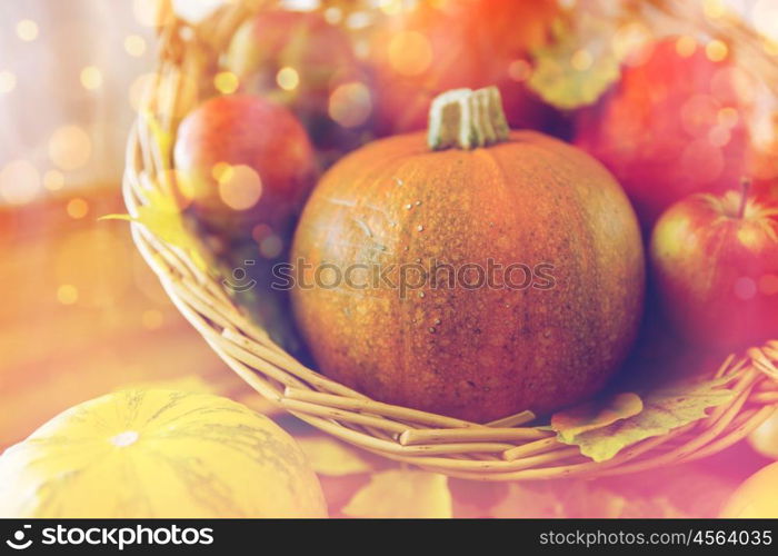 harvest, season, advertisement and autumn concept - close up of pumpkins in wicker basket with leaves on wooden table at home