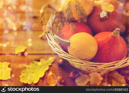 harvest, season, advertisement and autumn concept - close up of pumpkins in wicker basket with leaves on wooden table at home