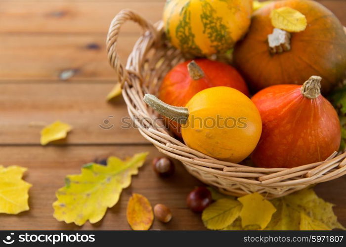 harvest, season, advertisement and autumn concept - close up of pumpkins in wicker basket with leaves on wooden table at home