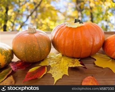 harvest, season and autumn concept - close up of pumpkins and leaves on wooden table over natural background
