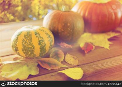 harvest, season and autumn concept - close up of pumpkins and leaves on wooden table over natural background