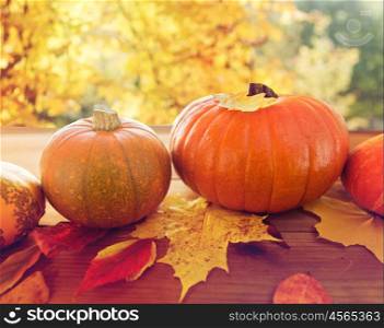 harvest, season and autumn concept - close up of pumpkins in wicker basket with leaves on wooden table over natural background