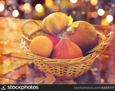 harvest, season, halloween and autumn concept - close up of pumpkins in wicker basket with leaves on wooden table over holidays lights