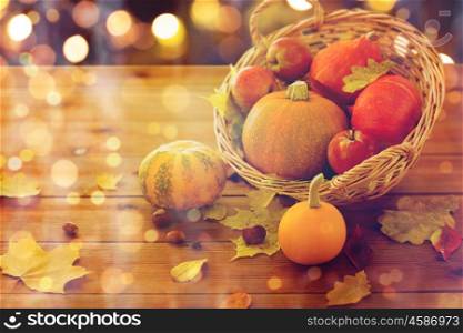 harvest, season, halloween and autumn concept - close up of pumpkins in wicker basket with leaves on wooden table over holidays lights