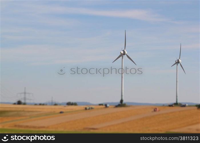 harvesting a barley field with two wind turbines nearby, focus on wind turbine. harvest