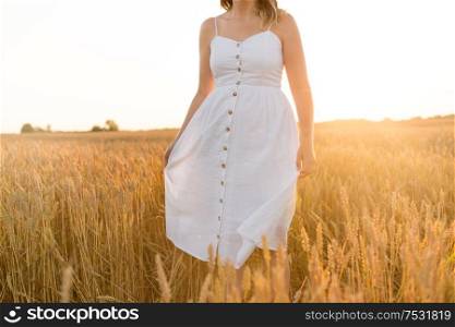 harvesting, nature, agriculture and prosperity concept - young woman in white dress walking through ripe wheat spickelets on cereal field. woman in white dress walking along cereal field