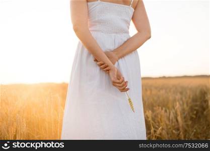 harvesting, nature, agriculture and prosperity concept - young woman in white dress on cereal field holding ripe wheat spickelet in her hand. woman on cereal field holding ripe wheat spickelet