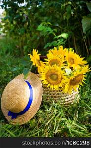 Hat, a bouquet of sunflowers lies in a straw bag on the green grass. Close-up.. Hat, a bouquet of sunflowers lies in a straw bag on the green grass.
