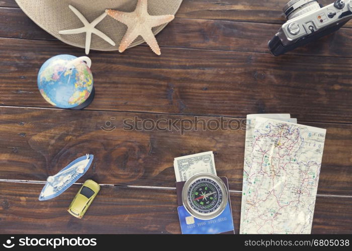 hat, compass, passport, credit card, banknote money, globe, camera, map, car ship and starfish figurine on wooden table for use as traveling concept (vintage tone and selected focus)