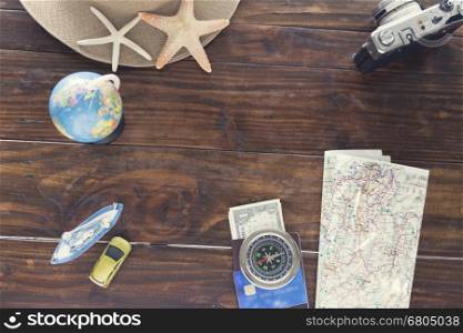 hat, compass, passport, credit card, banknote money, globe, camera, map, car ship and starfish figurine on wooden table for use as traveling concept (vintage tone and selected focus)