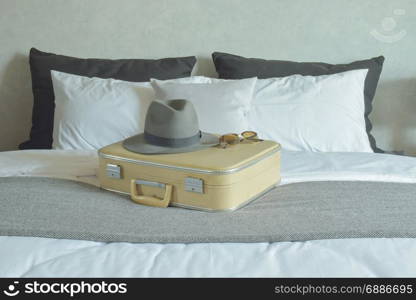 Hat, sunglasses and vintage travel bag setting on bed