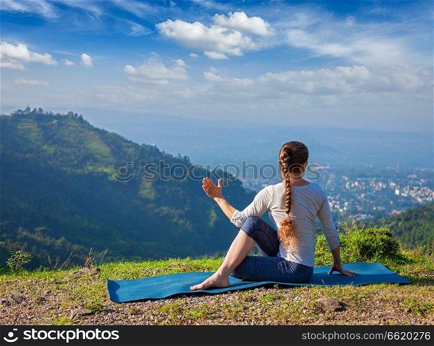 Hatha yoga outdoors - sporty fit woman doing yoga asana Parivrtta Marichyasana  or ardha matsyendrasana  -  seated spinal twist outdoors in mountains in the  morning. Woman doing Hatha yoga asana outdoors