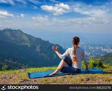 Hatha yoga outdoors - sporty fit woman doing yoga asana Parivrtta Marichyasana  or ardha matsyendrasana  -  seated spinal twist outdoors in mountains in the  morning. Woman doing Hatha yoga asana outdoors
