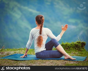 Hatha yoga outdoors - sporty fit woman doing yoga asana Parivrtta Marichyasana  or ardha matsyendrasana  -  seated spinal twist outdoors in mountains. Vintage retro effect filtered hipster style image.. Woman practices yoga asana outdoors