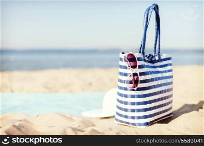 hats and summer concept - white straw hat, sunglasses and bag lying in the sand on the beach