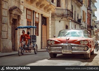 Havana, Cuba - March 22, 2019: Shiny retro car parked on the street and bicycle taxi driver riding by