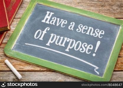 Have a sense of purpose advice or reminder on a slate blackboard with a white chalk and a stack of books against rustic wooden table
