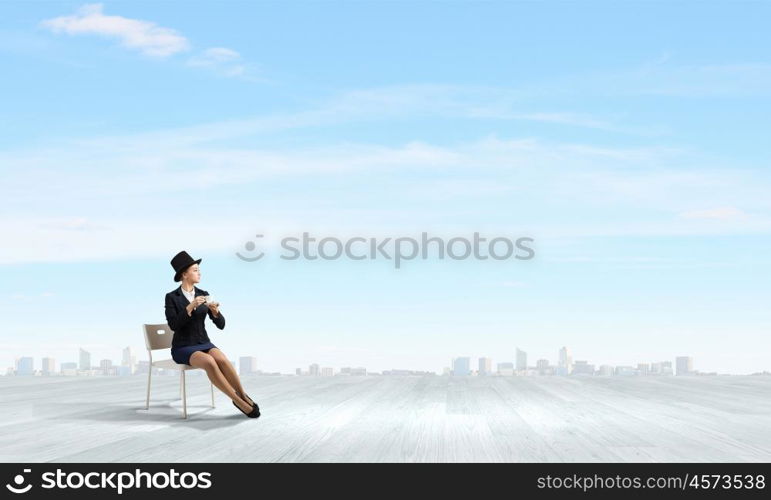 Have coffee break. Pretty girl wearing retro hat siting on chair with cup in hand