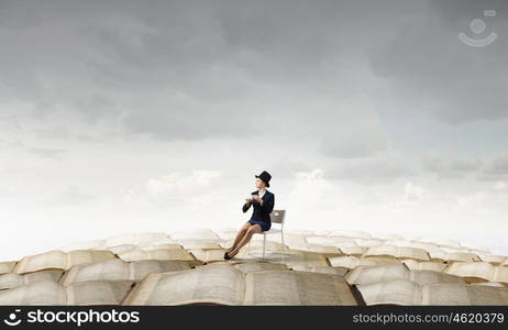 Have coffee break. Pretty girl wearing retro hat siting on chair with cup in hand