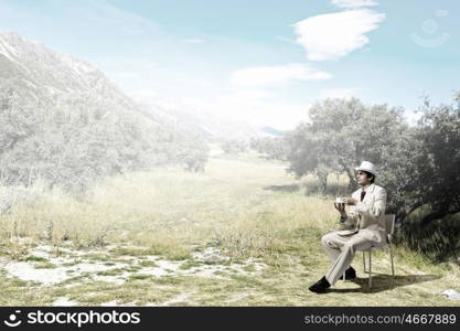 Have coffee break. Young businessman in white hat and suit sitting in chair