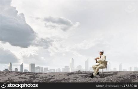 Have coffee break. Young businessman in white hat and suit sitting in chair