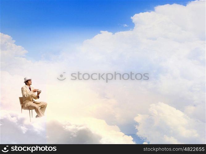 Have coffee break. Young businessman in white hat and suit sitting in chair