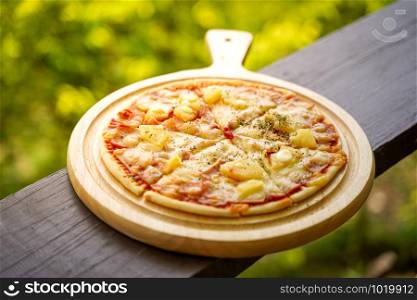 hawaiian pizza on wood table with green bokeh background