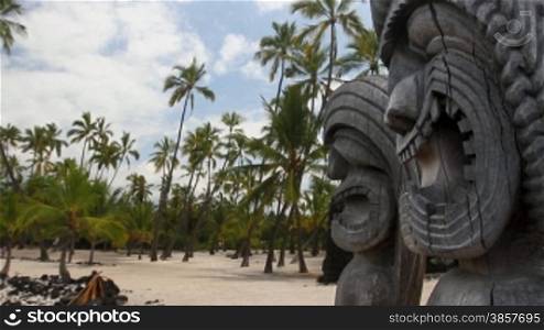 Hawaiian Tikis in the foreground with a sandy palm tree beach in the background
