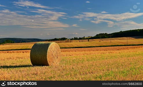 Hay bail harvesting in golden field landscape. Summer Farm Scenery with Haystack on the background of Beautiful Sunset.