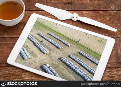 hay bales in Nebraska Sandhills, reviewing aerial image on a digital tablet with a cup of tea