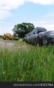 Hay bales wrapped in black plastic being moved by the farmer