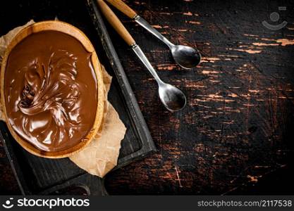 Hazelnut butter in a plate on a cutting board with paper. Against a dark background. Top view. High quality photo. Hazelnut butter in a plate on a cutting board with paper.